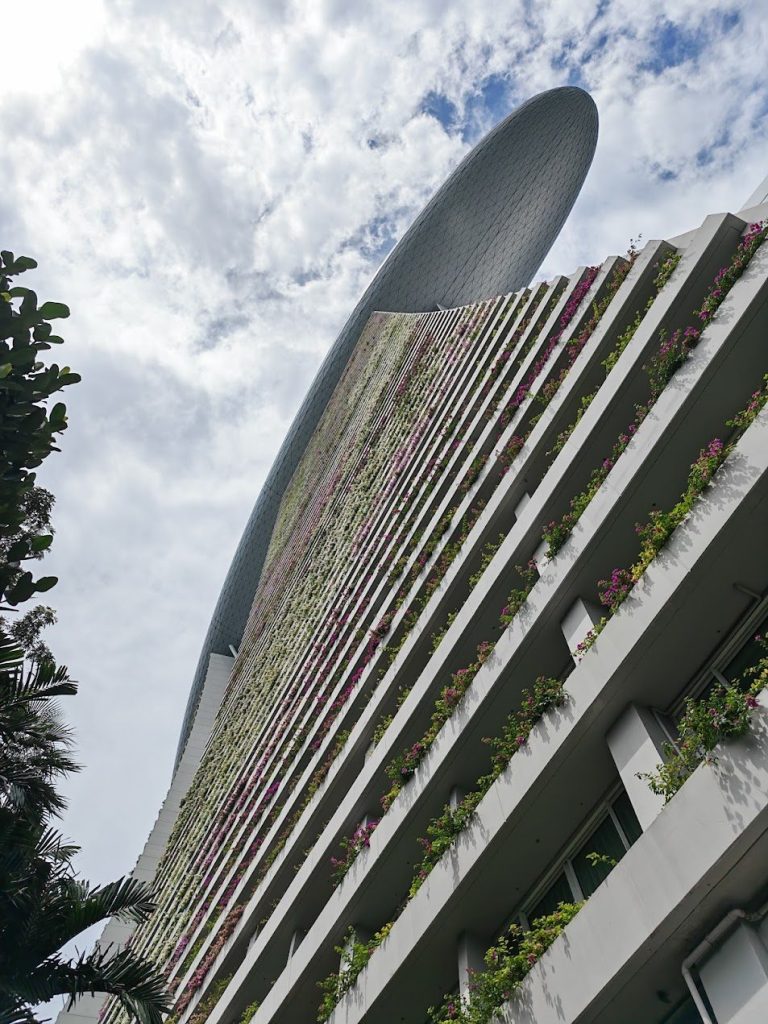 Tall planted tower facade with balconies, greenery, and vertical building lines in Singapore.