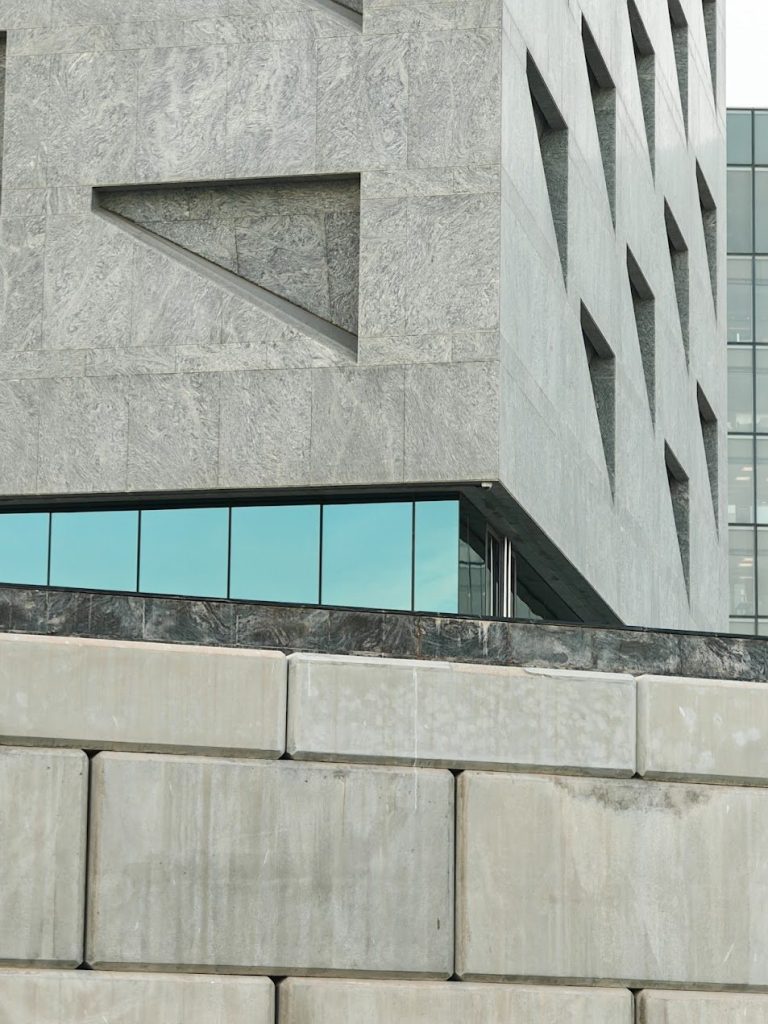 Stone facade with angled window openings, glass, and precise geometric cladding.