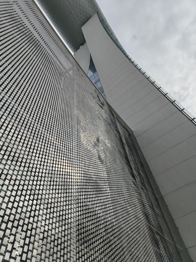 Metal mesh building skin catching light, shadow, and reflection along a facade edge.
