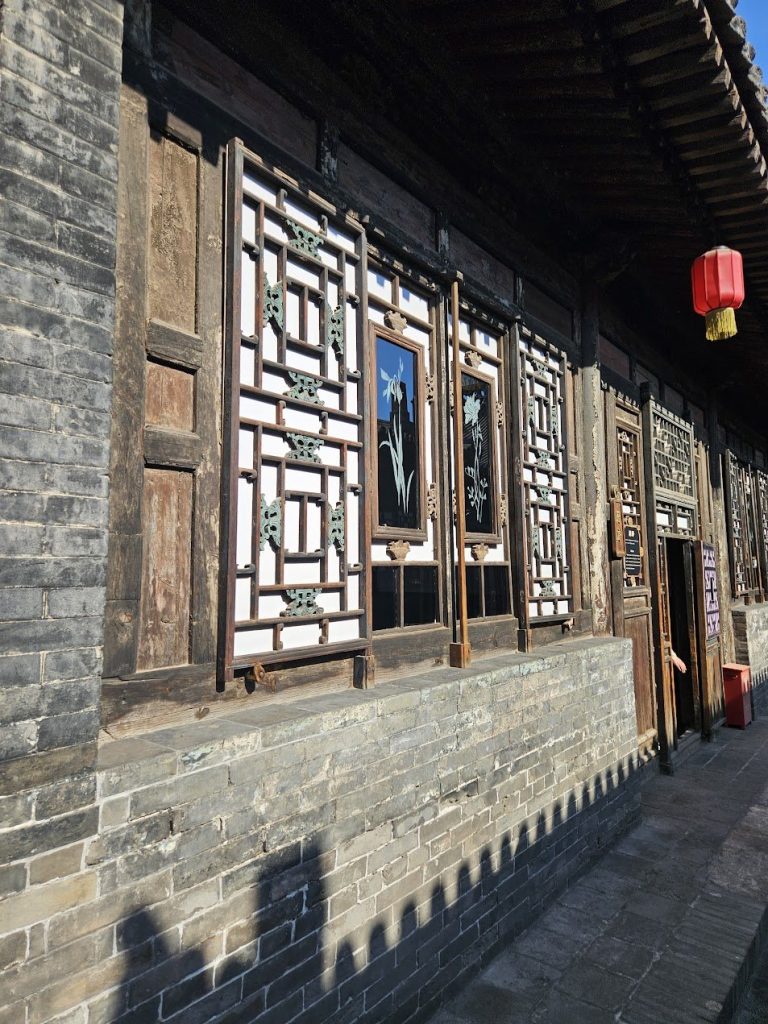 Timber windows, brick wall, and shadow forming a layered traditional facade.
