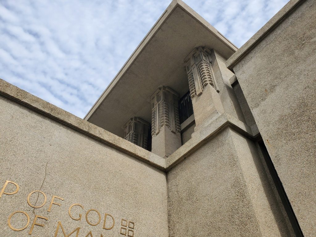Heavy concrete corner with recessed openings, layered mass, and textured surface.