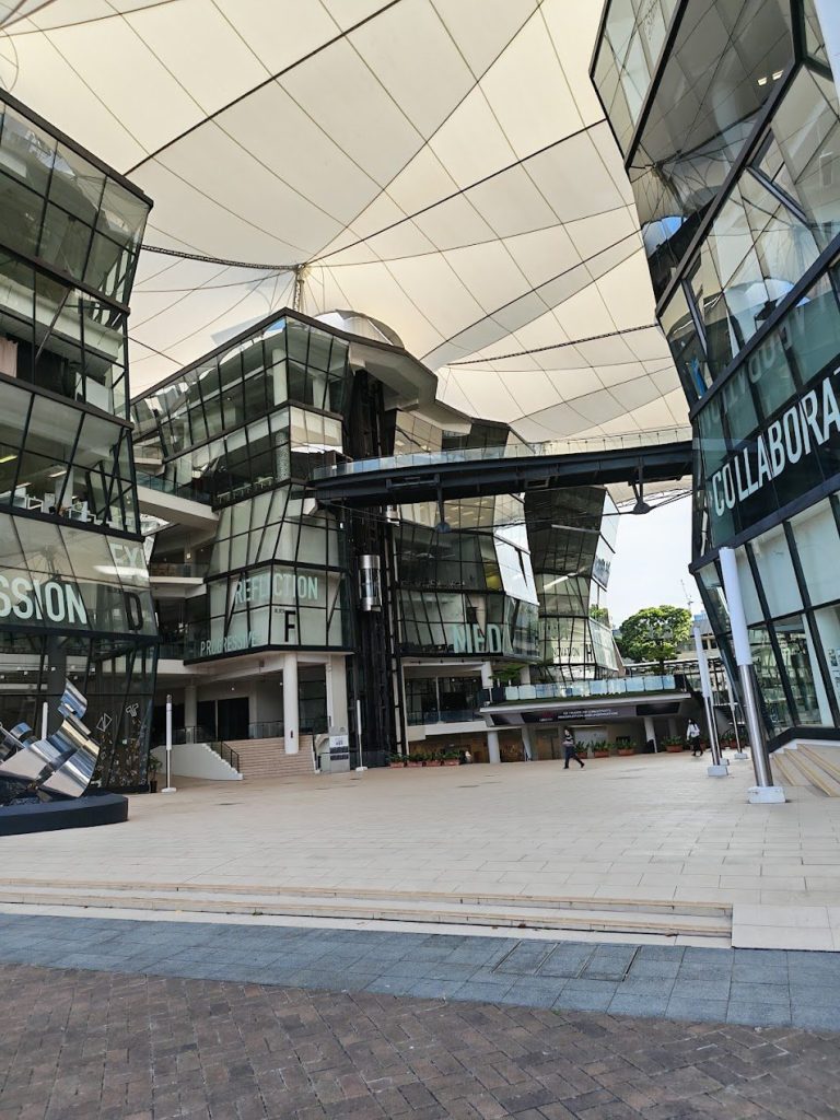 Glass buildings and stretched canopy shaping an open civic plaza in Singapore.