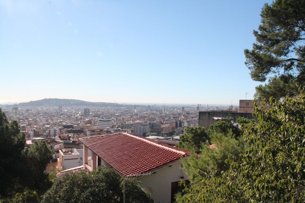 Rooftops, trees, and city horizon spreading into a broad Barcelona panorama.