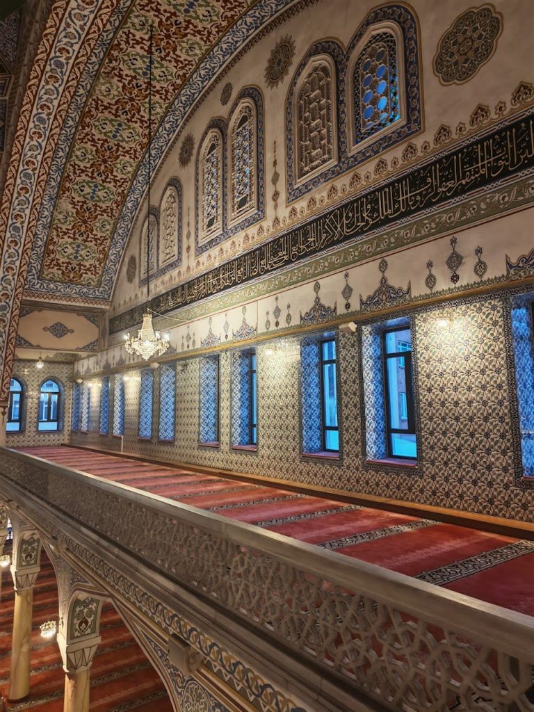 Mosque gallery hall with patterned walls, blue windows, chandeliers, and layered height.