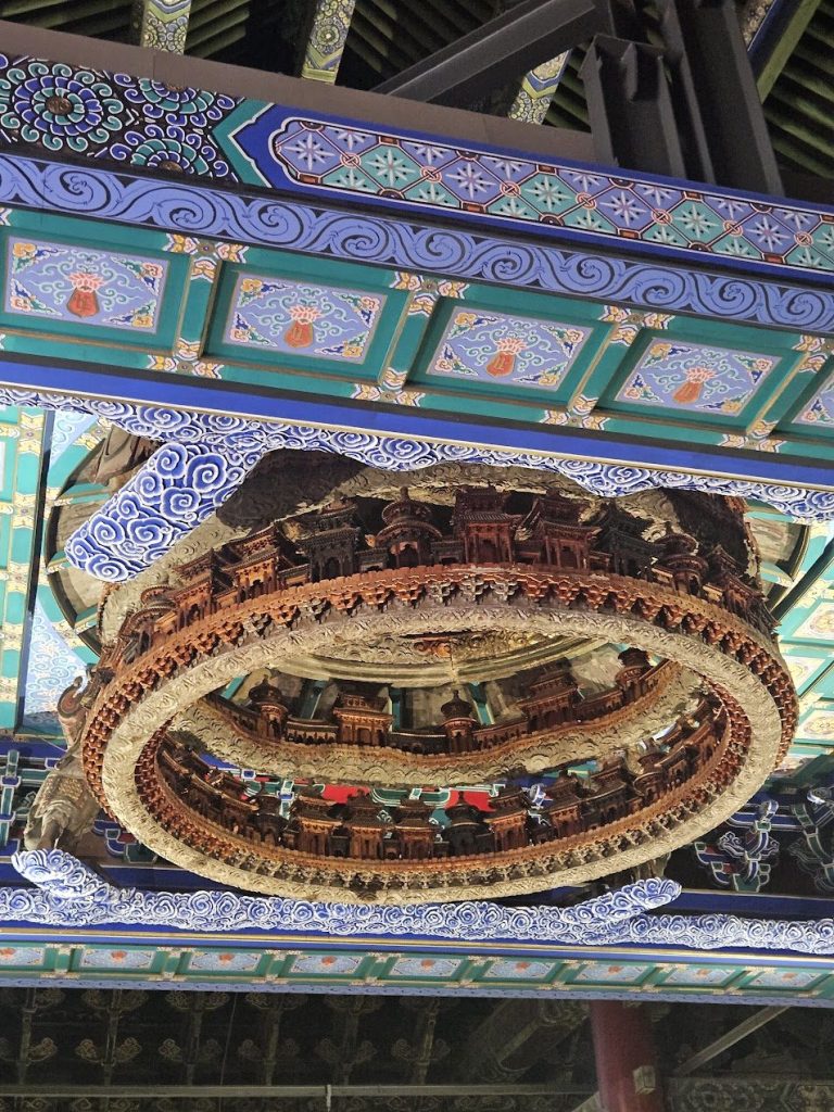 Painted ceiling ornament with layered colour, craft, and suspended carved detail.
