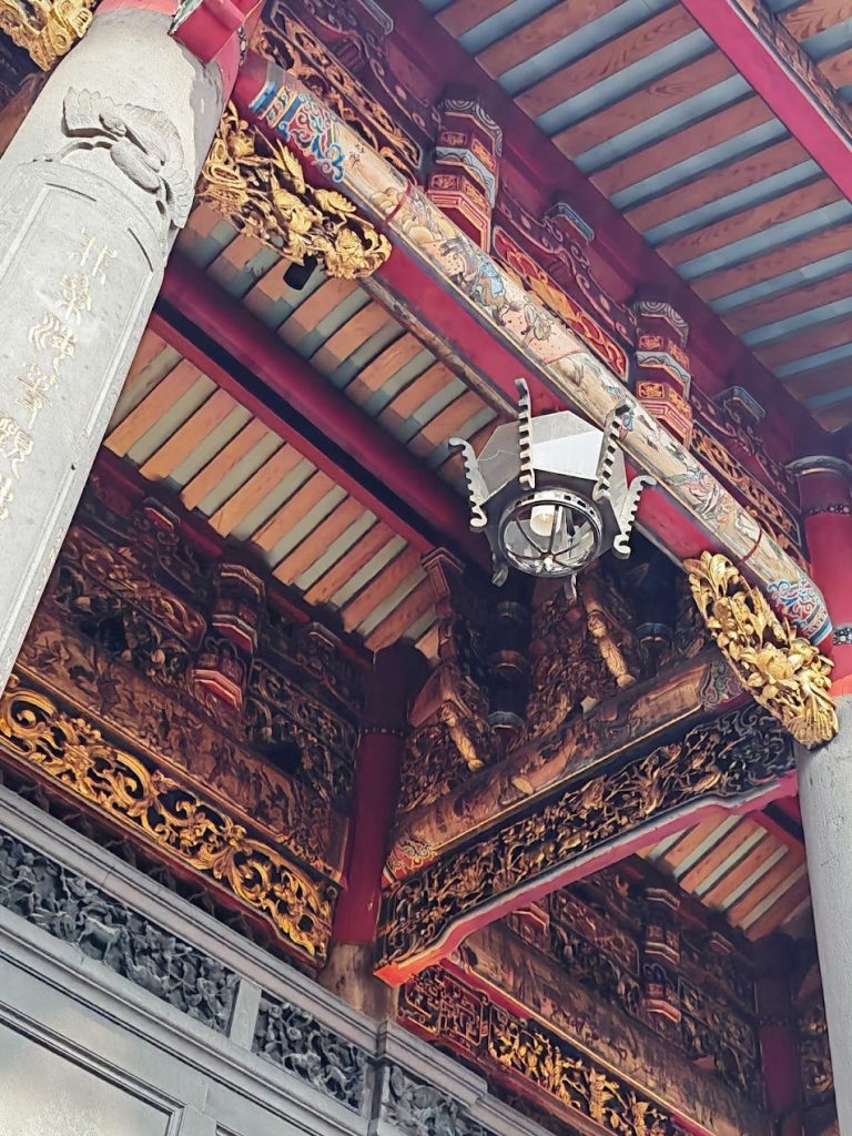 Richly carved eave corner with ornament, red structure, gold detail, and warm shadow.